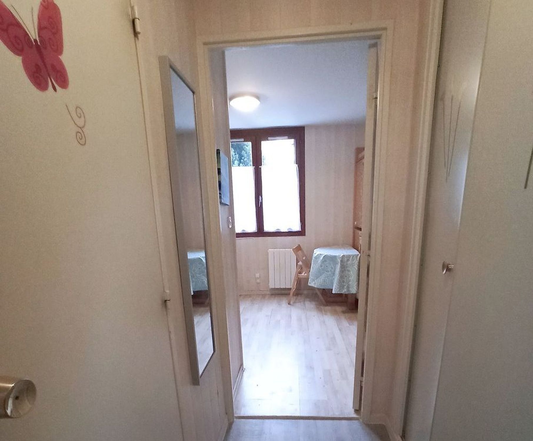 A narrow hallway leading to a room with a window and a table with a tablecloth.