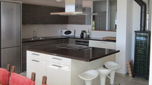 Eine moderne Küche mit Edelstahl-Kühlschrank, Mikrowelle und eingebautem Backofen. Eine große Kochinsel mit Barhocker und schwarzer Arbeitsplatte vorhanden.
