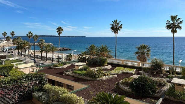Un hotel sulla costa con palme, una spiaggia e un cielo azzurro limpido.