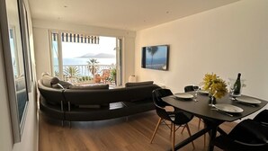 Un soggiorno moderno con un divano ad arco, un tavolo da pranzo per due persone e una grande finestra con vista sul mare.