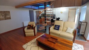 Ein Wohnzimmer mit Sofa, Sessel, Couchtisch aus Holz und einer Treppe mit Metallgeländer.