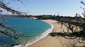 Ein Strand mit klarem, blauem Wasser und sandigem Ufer, umgeben von Hügeln und spärlicher Vegetation.