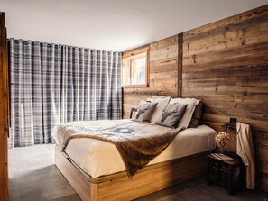 A wooden bed with a headboard, a plaid curtain, and a small bedside table with a vase of flowers.