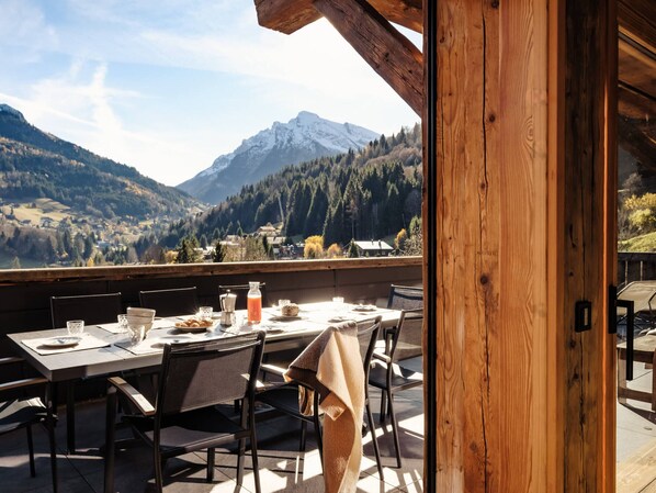 Ein Holzbalkon mit Esstisch, der auf eine gebirgige Landschaft blickt.