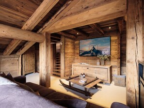 Een houten interieur met een bank, een houten bijzettafeltje, een aan de muur bevestigde televisie en een houten trap.