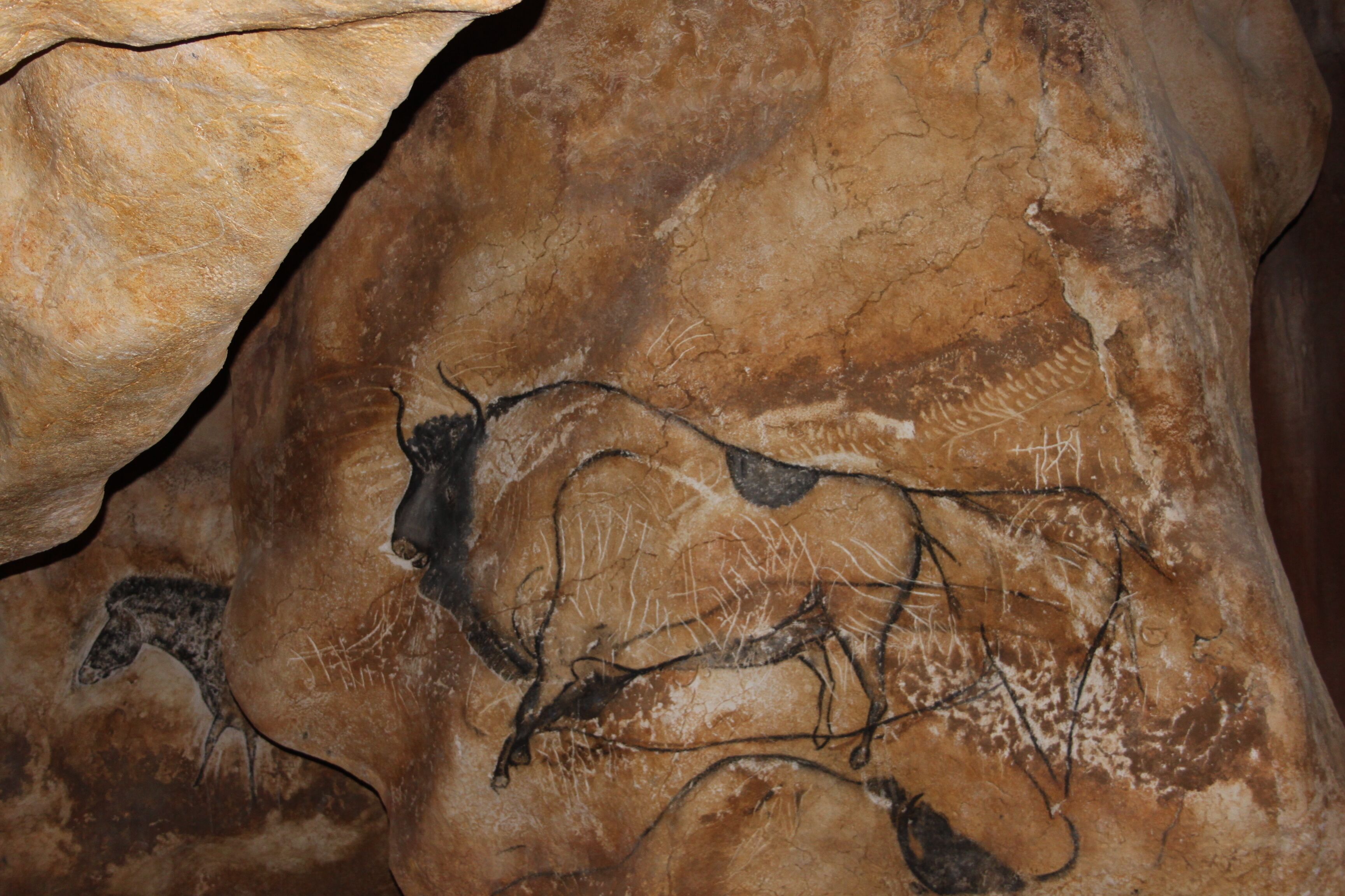 A cave interior with ancient cave paintings of animals and human figures.