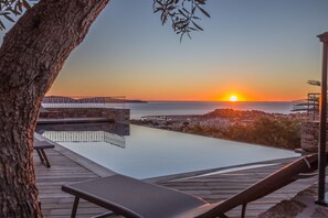 A rooftop infinity pool with a view of the sunset over the sea, wooden deck, and lounge chairs. - VILLA SOLEIL D'OR GOLFE DE ST TROPEZ4*, swimming pool at 29° all year round, 180° view (Cavalaire-sur-Mer)