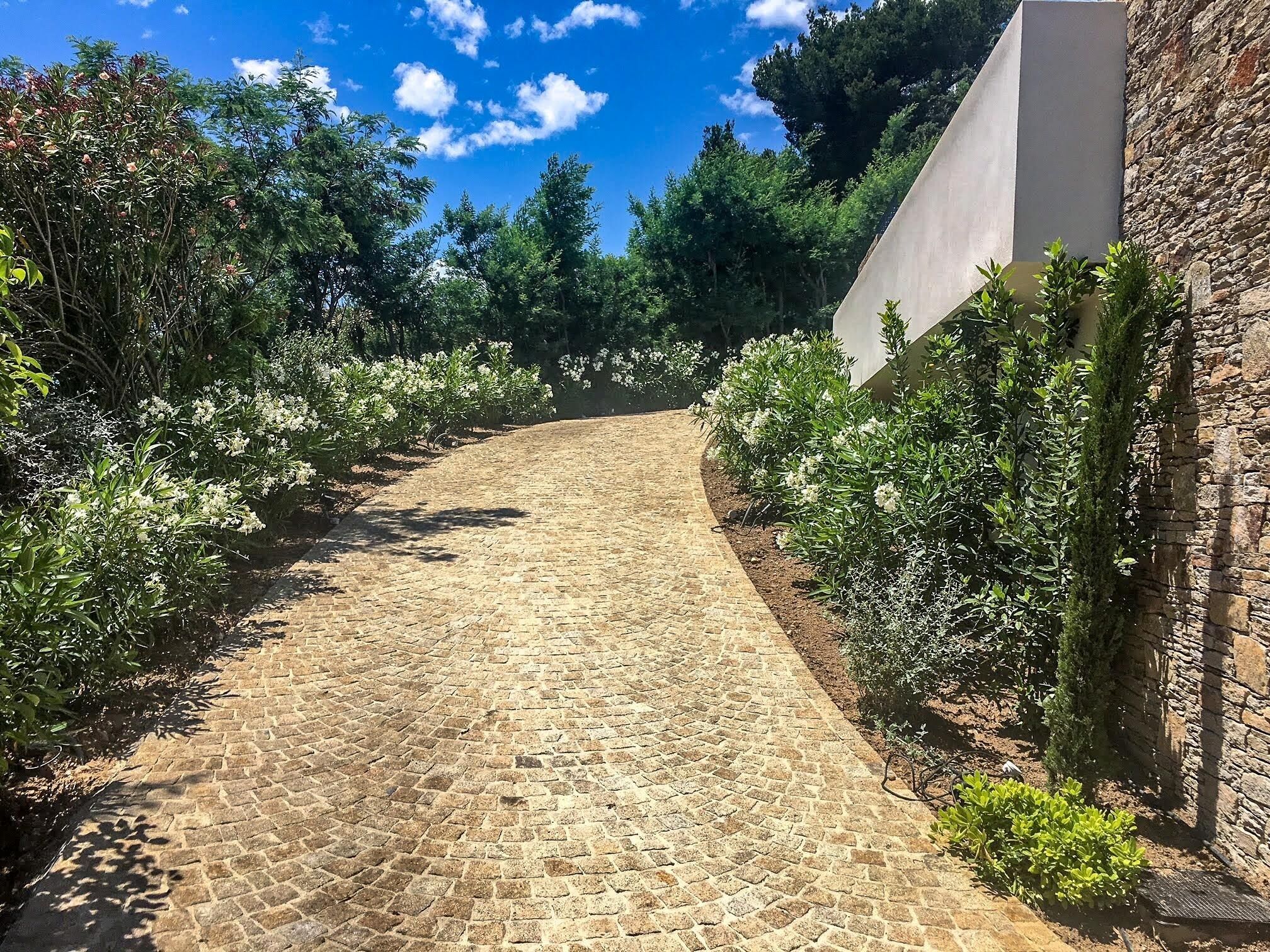 Ein Kopfsteinpflasterweg, gesäumt von üppiger Vegetation und einer Steinmauer.