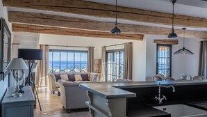 A modern kitchen with a large island, a dining area with a sofa, and a view of the sea. - VILLA SOLEIL D'OR GOLFE DE ST TROPEZ4*, swimming pool at 29° all year round, 180° view (Cavalaire-sur-Mer)
