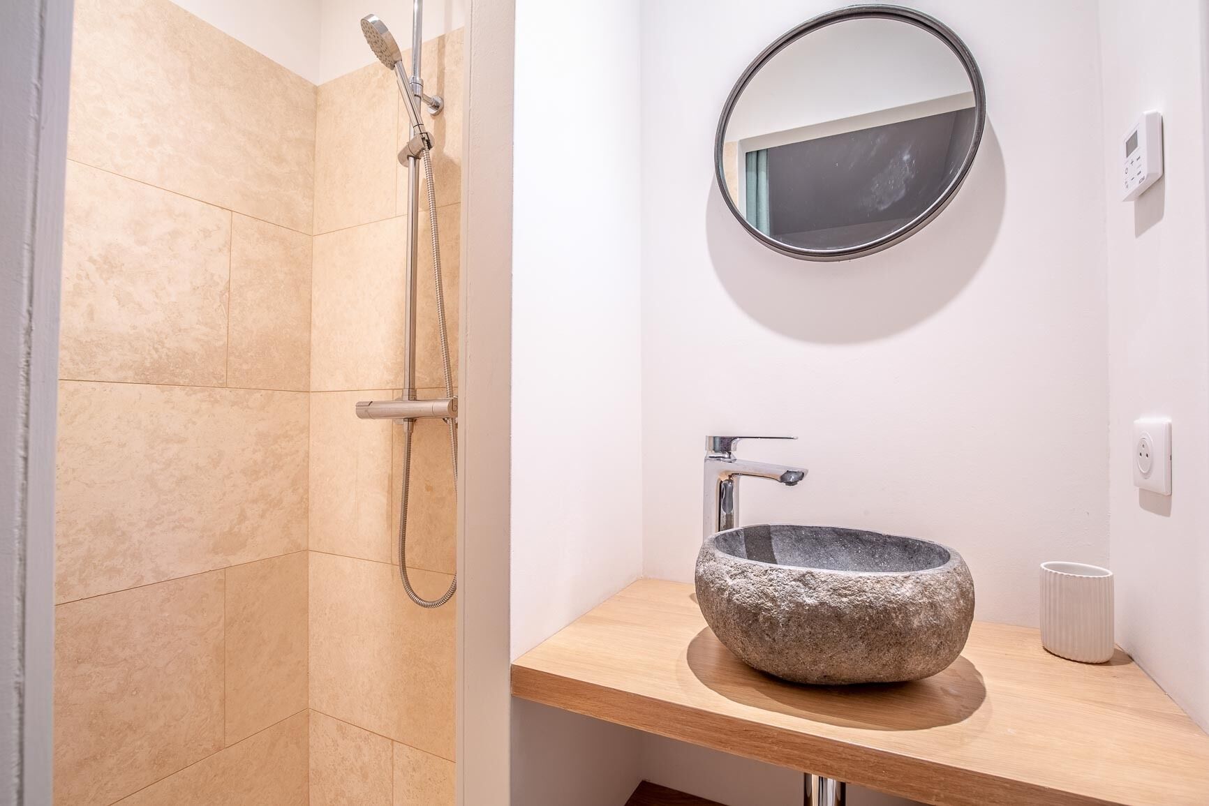A bathroom with a stone sink, a handheld showerhead, and a round mirror.