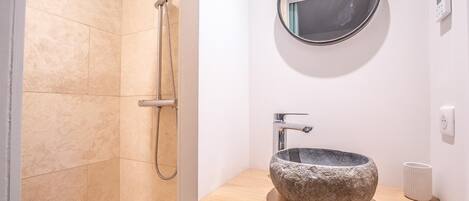 A bathroom with a stone sink, a handheld showerhead, and a round mirror.