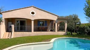 Ein zweistöckiges Haus mit Pool, einer überdachten Terrasse und einem kleinen Garten.