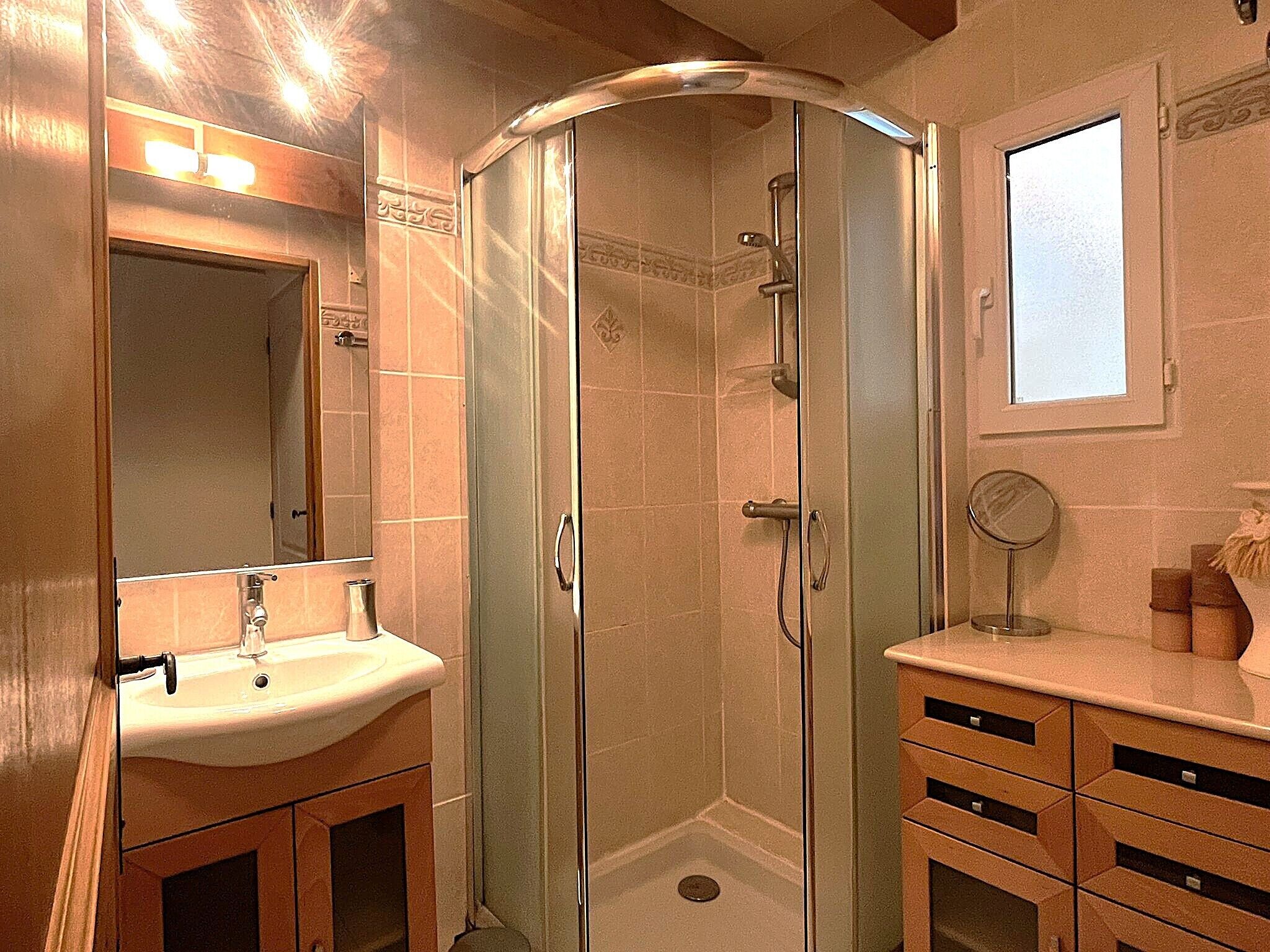 A bathroom with a glass-enclosed shower, a sink, a mirror, and wooden cabinets.