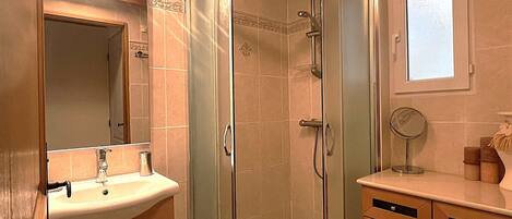 A bathroom with a glass-enclosed shower, a sink, a mirror, and wooden cabinets.