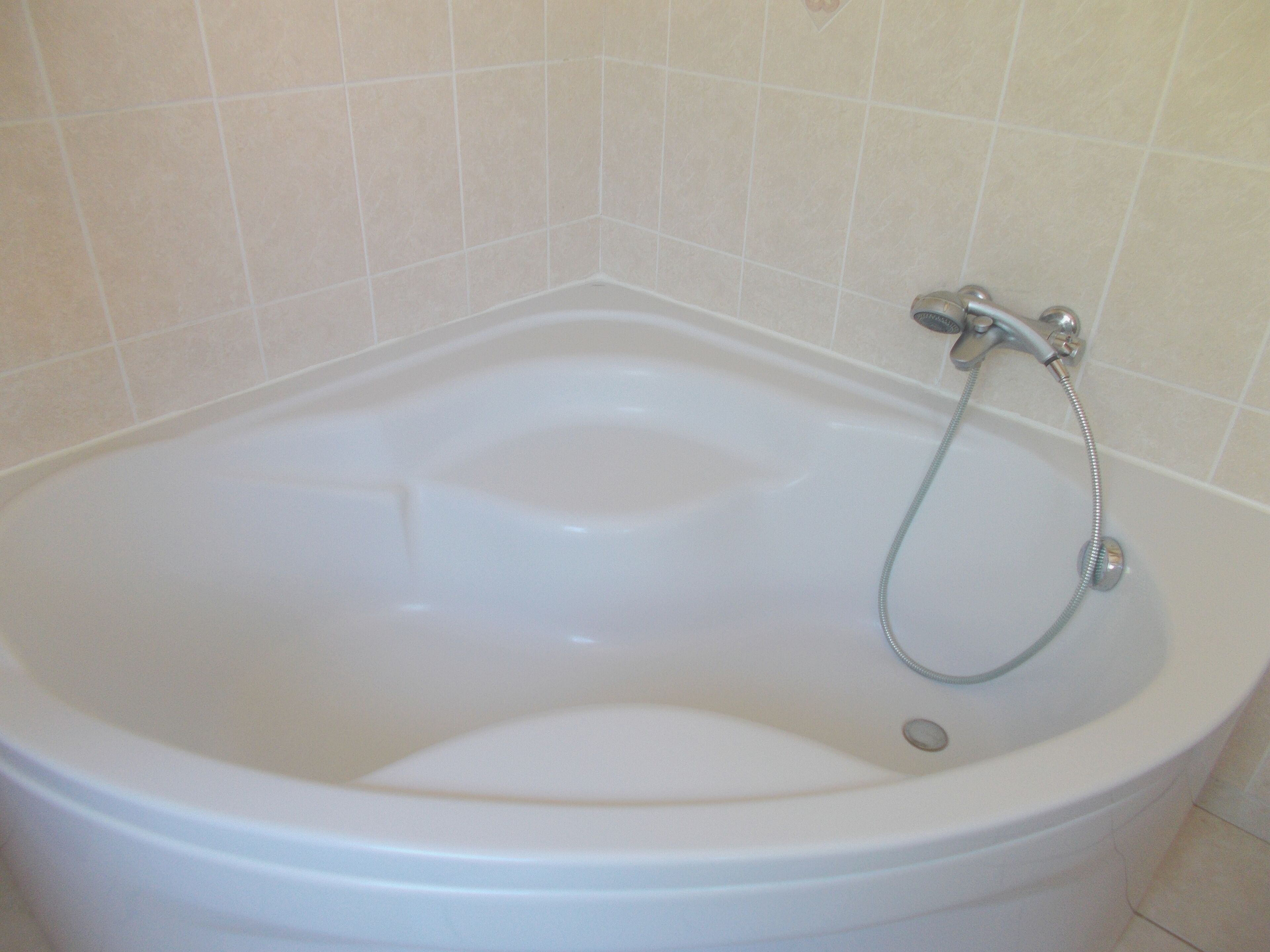 A white bathtub with a shower head and hose, set against a tiled wall.