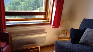 Una habitación acogedora con una mesa de madera, un sofá, un ventanal con vistas a montañas y un radiador.