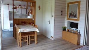 A compact kitchen with wooden cabinets, a dining table with chairs, a TV on a wooden stand, and a door with a number. - holidays in GERARDMER 100m from the lake (Gérardmer)