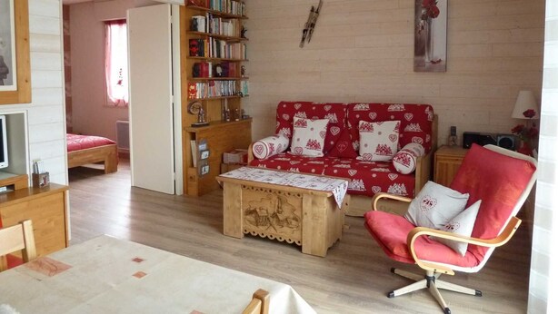 A cozy living room with a wooden bookshelf, a red sofa with heart patterns, a wooden coffee table, and a red armchair. - holidays in GERARDMER 100m from the lake (Gérardmer)