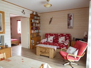 Een gezellige woonkamer met een houten boekenkast, een rode bank met hartjesprint, een houten salontafel en een rode fauteuil.