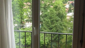 A balcony with a wooden chair, a table with a floral tablecloth, and a view of a green landscape with trees and houses. - holidays in GERARDMER 100m from the lake (Gérardmer)