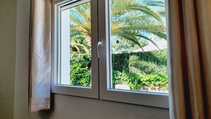 Une fenêtre donnant sur un jardin, avec des palmiers et différentes espèces de plantes.