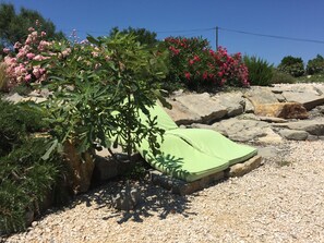 Ein Garten mit einer grünen Sitzgelegenheit im Freien, umgeben von Steinen und verschiedenen blühenden Pflanzen.