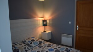 Ein Schlafzimmer mit einem Bett, einem Nachttisch mit Lampe, einem Heizkörper und einer Holztür.