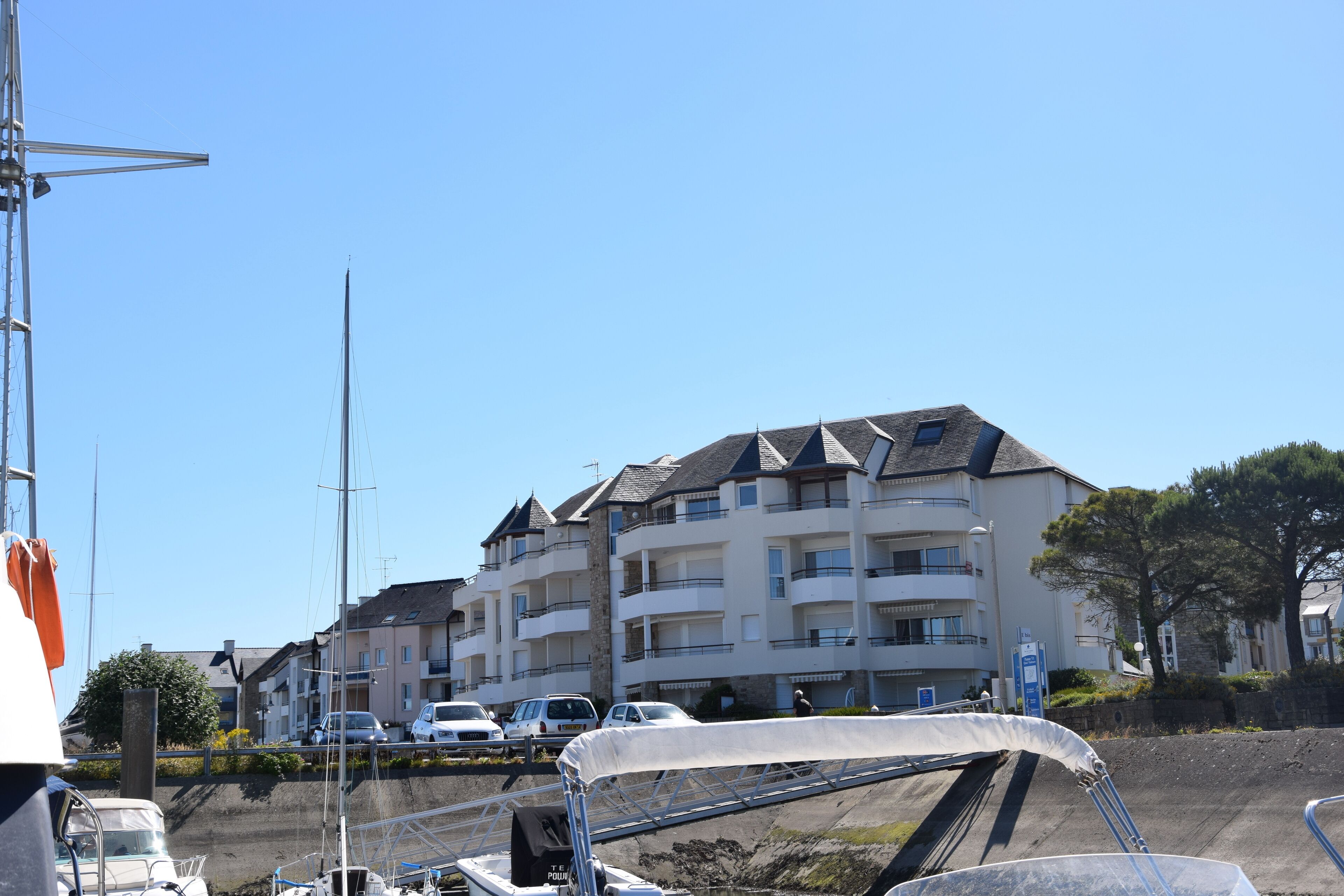 A multi-story building with balconies, a marina with boats, and a clear blue sky.