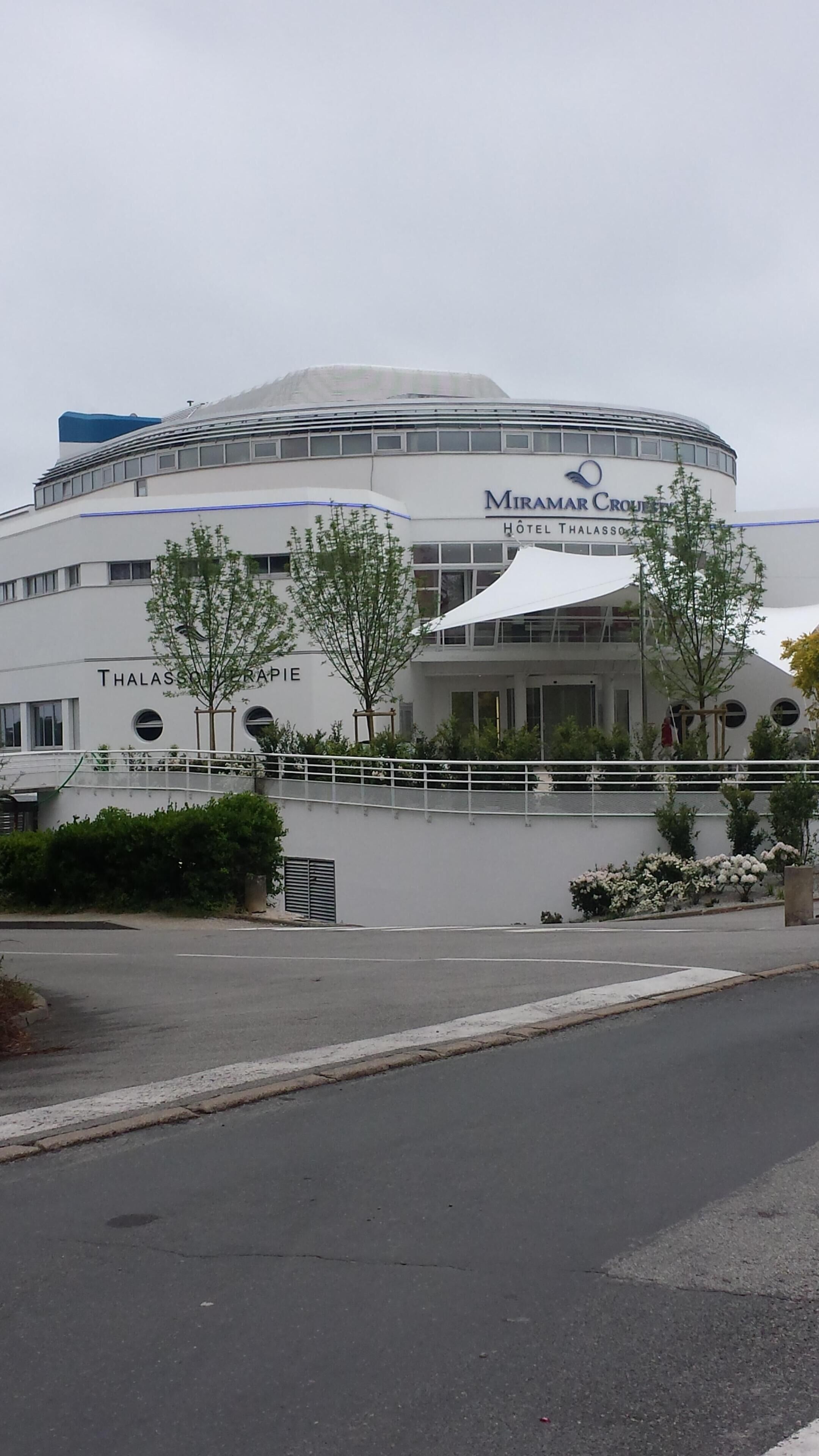 Un edificio moderno con estructura circular, llamado 'Miramar Cruise Hotel Thalasso', que presenta un balcón y un área cubierta con árboles.