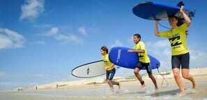 Trois personnes courent sur une plage en portant des planches de surf.