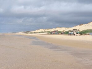 Ein sandiger Strand mit Dünen und im Hintergrund Gebäuden mit Graffiti.