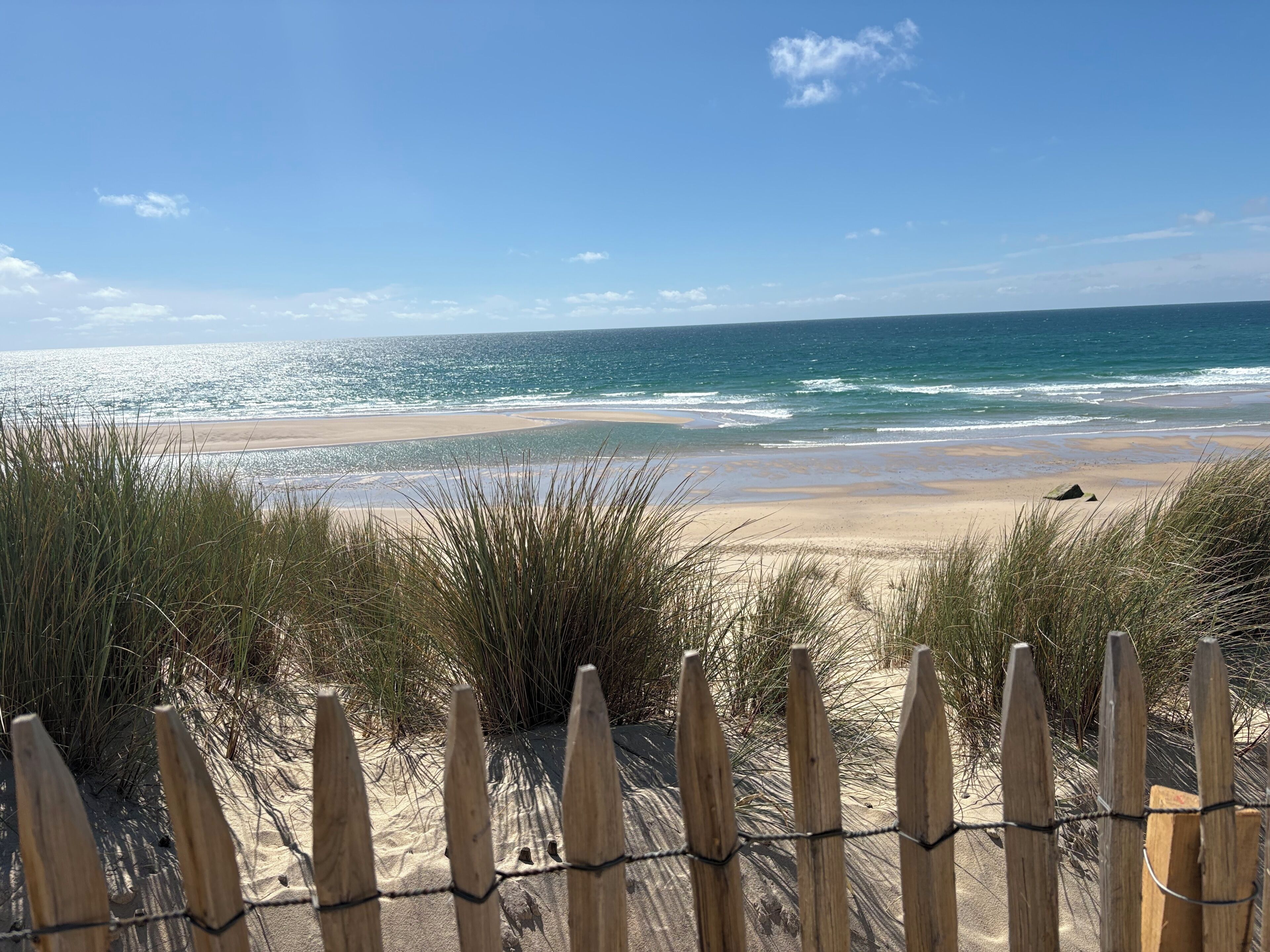 A beach with a wooden fence in the foreground and a clear view of the ocean.