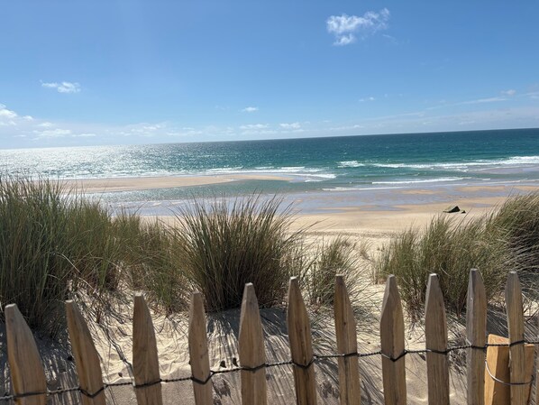 A beach with a wooden fence in the foreground and a clear view of the ocean.