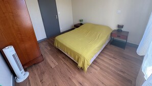 Ein Schlafzimmer mit Bett, Schrank, Tür, Nachttisch mit Lampe und Heizung.