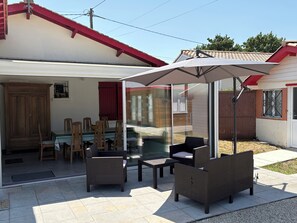 A patio area with wicker furniture, a glass door leading to a room, and a red roof.