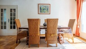 A dining area with wicker chairs, a round table, and a framed picture on the wall.