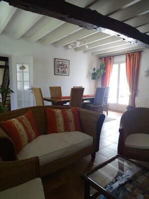 A living room with a sofa, chairs, a dining table, and a glass coffee table. - Le Gîte : Une parenthèse de sérénité dans un authentique (Azay-sur-Indre)