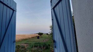 A view through blue doors to a rural landscape with a field and a small tree. - IN FRONT OF THE SEA. ALMOST PENERF ISLAND. WIRELESS. (Damgan)