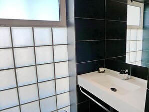 Een badkamer met een wit wastafel, donkere tegels en een spiegel.