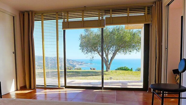 Une pièce dotée d’une grande porte-fenêtre coulissante donnant sur un balcon avec vue sur la mer et un arbre.