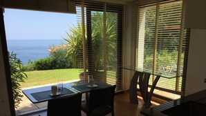 Un espace repas comprenant une table et des chaises, une cloison en verre et une vue sur la mer grâce à de grandes fenêtres.