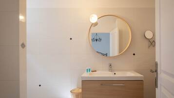 A modern bathroom with a round mirror, white tiles, a wooden vanity, and a light fixture.