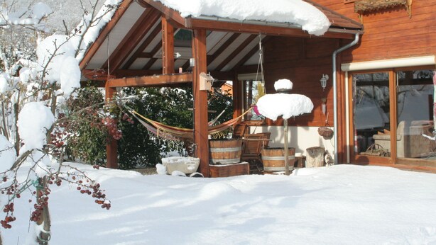 A wooden cabin with a covered porch, snow accumulation, and outdoor furniture. - GUEST ROOM 2 PEOPLE IN PRETTY SAVOYARD HOUSE (Mercury)