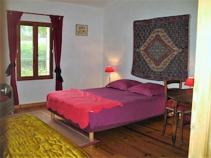 Une chambre à coucher avec un lit, deux lampes de chevet, une fenêtre avec des rideaux, une tapisserie au mur et un plancher en bois.