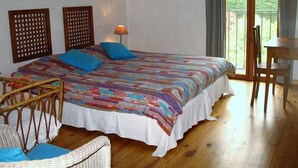A bedroom with a bed, a chair, a table, and a view of greenery through a window.