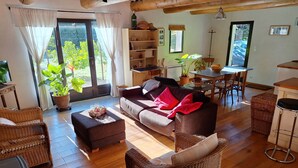 A cozy living room with a sofa, ottoman, wicker chairs, and a dining area with a table and chairs.