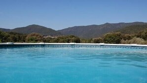 A swimming pool with clear blue water, surrounded by greenery and mountains in the background.