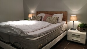 Una cama bien hecha con ropa blanca, dos lámparas de noche y una planta pequeña en la mesita.