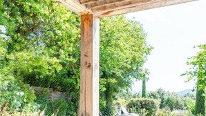 A wooden table with a kettle and bowls, a pool, and a pergola with a view of trees and mountains.