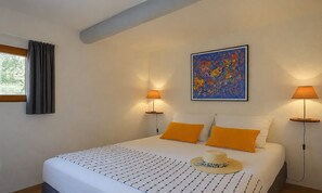 A bedroom with a bed, two bedside lamps, a painting, and a window with curtains.